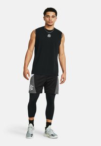 Schwarzes ärmelloses Shirt, schwarze Shorts mit grauen Akzenten, schwarze Leggings und gemusterte Sneakers. Das Shirt und die Shorts haben ein Logo.