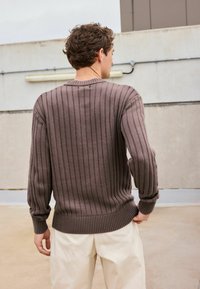 Pull en laine marron tricoté avec des côtes verticales, encolure ras du cou et manches longues. Présente une taille ajustée et un tissu texturé.