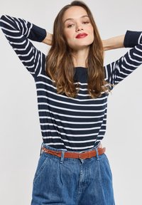 Mørkeblå og hvid stribet langærmet T-shirt, parret med højtaljede lys blå denimjeans og et brunt vævet læderbælte.