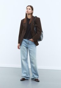Hnědý blazer, černá košile, světle modré široké džíny a hnědé kožené boty. Velká černá kabelka, hladké textury, neformální design.
