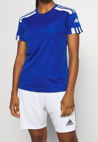 Blå idrottströja med vita detaljer, med korta ärmar, rund hals och tre ränder på axlarna. I kombination med vita shorts.