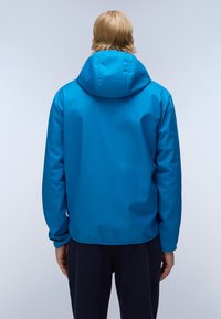 Blå hættejakke, glat tekstur, lange ærmer, elastiske manchetter, ensartet design, uden synlige lukninger eller logoer, båret over mørke bukser.