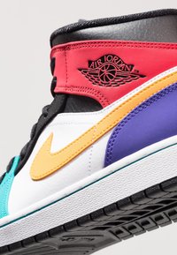 Gros plan d'une basket montante Air Jordan multicolore avec des panneaux rouges, noirs, blancs, jaunes, violets et bleu sarcelle, et le logo aile Air Jordan.
