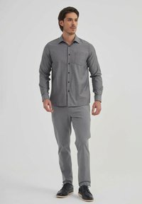 Chemise gris à manches longues avec une poche poitrine, associée à un pantalon gris clair assorti et des chaussures de ville noires.
