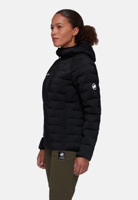 Giacca a vento nera con cappuccio, caratterizzata da un design trapuntato e tasche laterali. Toppa con logo sulla manica e polsini regolabili.