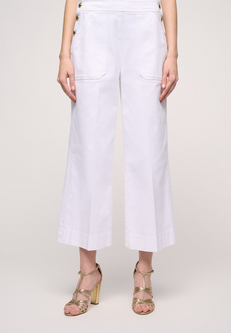 Pantaloni bianchi a gamba larga con tasche laterali e dettagli in bottone dorato, caratterizzati da una texture di cotone liscia e un design cropped e sartoriale.