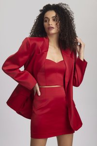 Piros selyem két részes szett, amely egy cropped bustier felsőt és egy magas derekú mini szoknyát tartalmaz, oversized blézerrel párosítva.