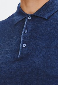 Granatowa koszulka polo z fakturowanej tkaniny, z klasycznym kołnierzykiem i trzema jasnoniebieskimi guzikami przy zapięciu.