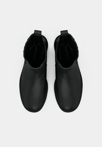 Musta pahkluu saapad, mis on valmistatud siledast nahast, ümarate varvaste ja elastsete küljeosadega, varustatud kandjal olevaga, mis võimaldab neid hõlpsasti jalga panna.