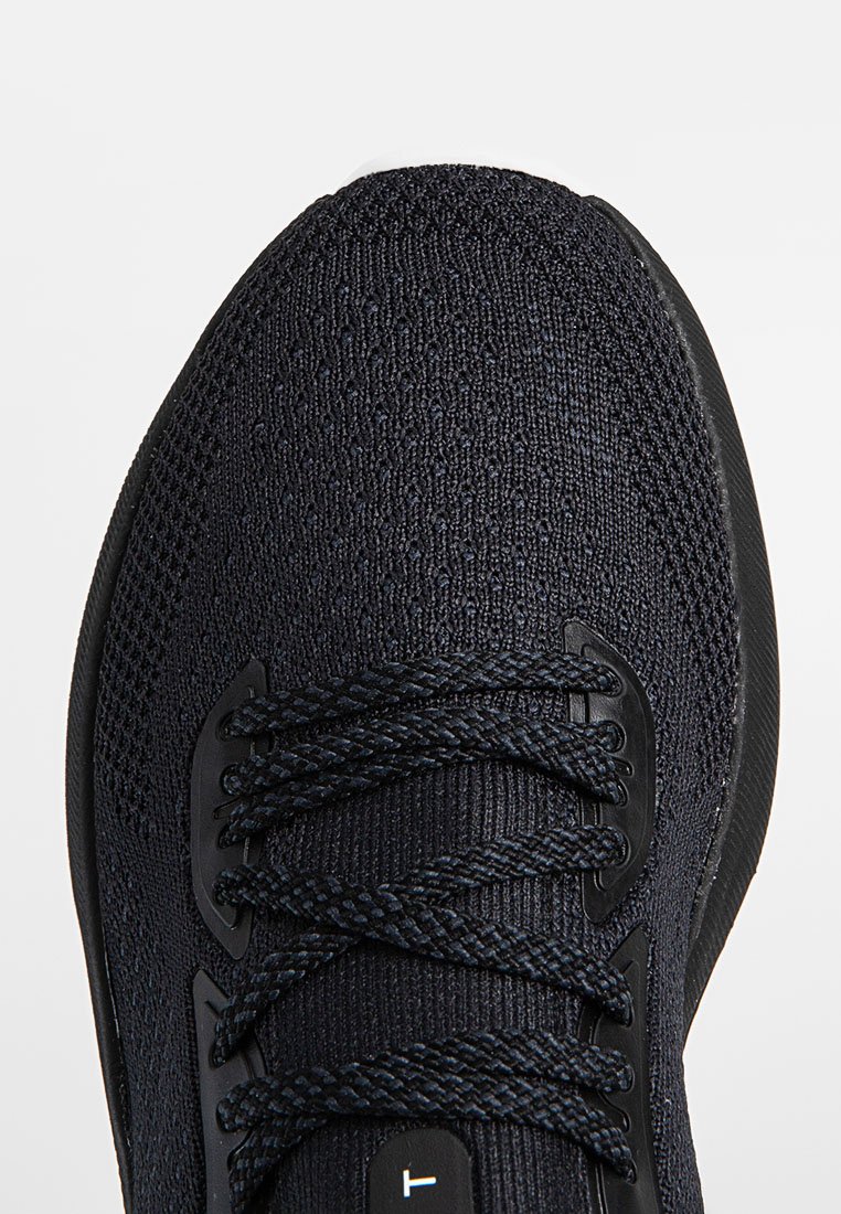 Acercamiento de una zapatilla deportiva de un intenso azul marino que presenta un upper de punto, cordones planos y una suela de goma negra lisa con acentos texturizados.