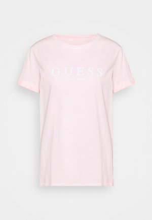 Jasnoróżowa koszulka z krótkim rękawem z białym napisem "GUESS EST. 1981" umieszczonym na środku klatki piersiowej, z okrągłym dekoltem i luźnym fasonem.