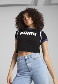 Camiseta negra corta con el logo de "PUMA" en blanco, acentos morados en las mangas, combinada con jeans de cintura alta en color azul claro. Textura de algodón suave.