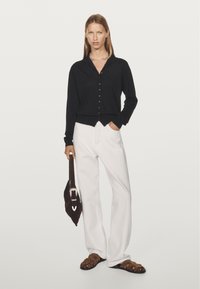 Black long-sleeve button-up cardigan, white wide-leg trousers, brown strappy sandals, and a dark bag with a silver buckle.