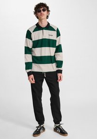 Långärmad polo skjorta med gröna och krämfärgade ränder, svart krage. Kombination med svarta joggers och svarta sneakers med ljusa detaljer.