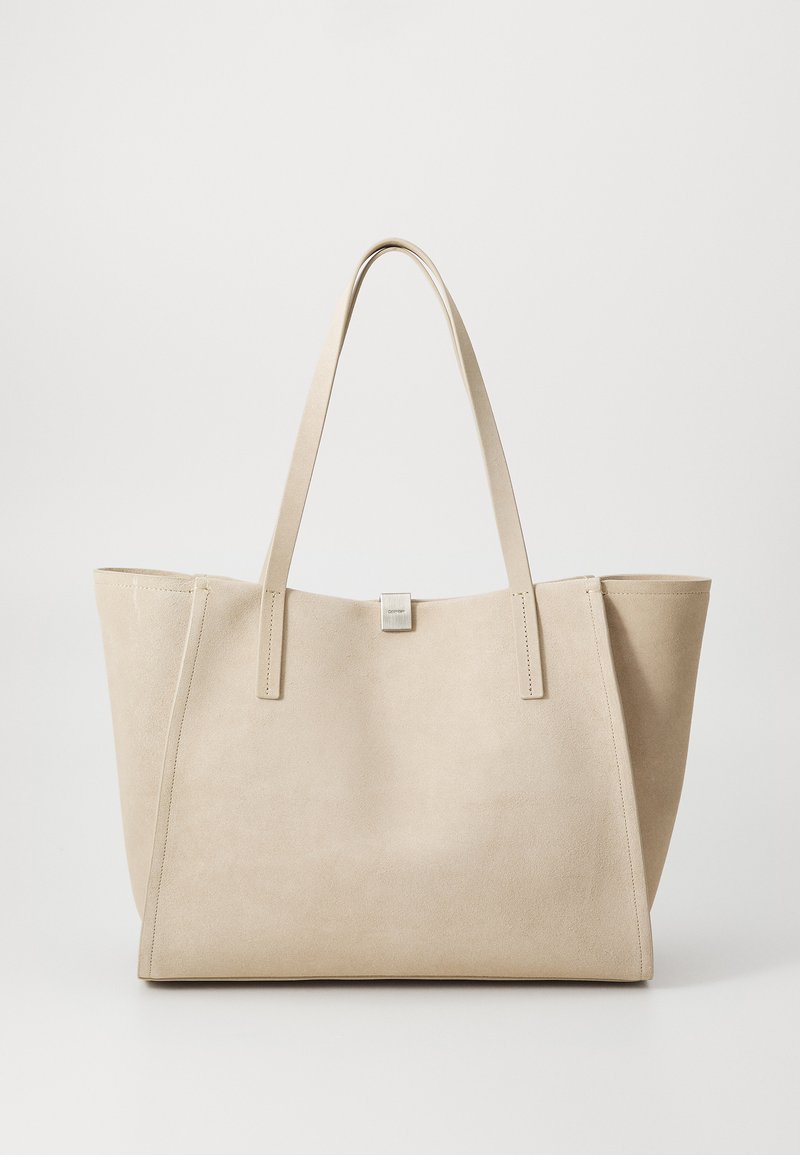 Beige ruskinds tote taske med doble flade håndtag, struktureret form og minimalistisk design. Bemærkelsesværdig syning og en lille metallisk logoaccent.
