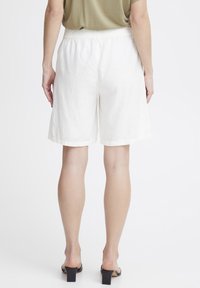 Bermuda en lin blanc avec une taille élastique, présentant une coupe décontractée et un ourlet retroussé. Texture lisse et légère.