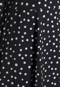 Schwarzer Stoff mit einem weißen und hellblauen gepunkteten Muster. Glatte Textur, geraffte Falten in der Nähe der Taille. Klassisches und vielseitiges Design.