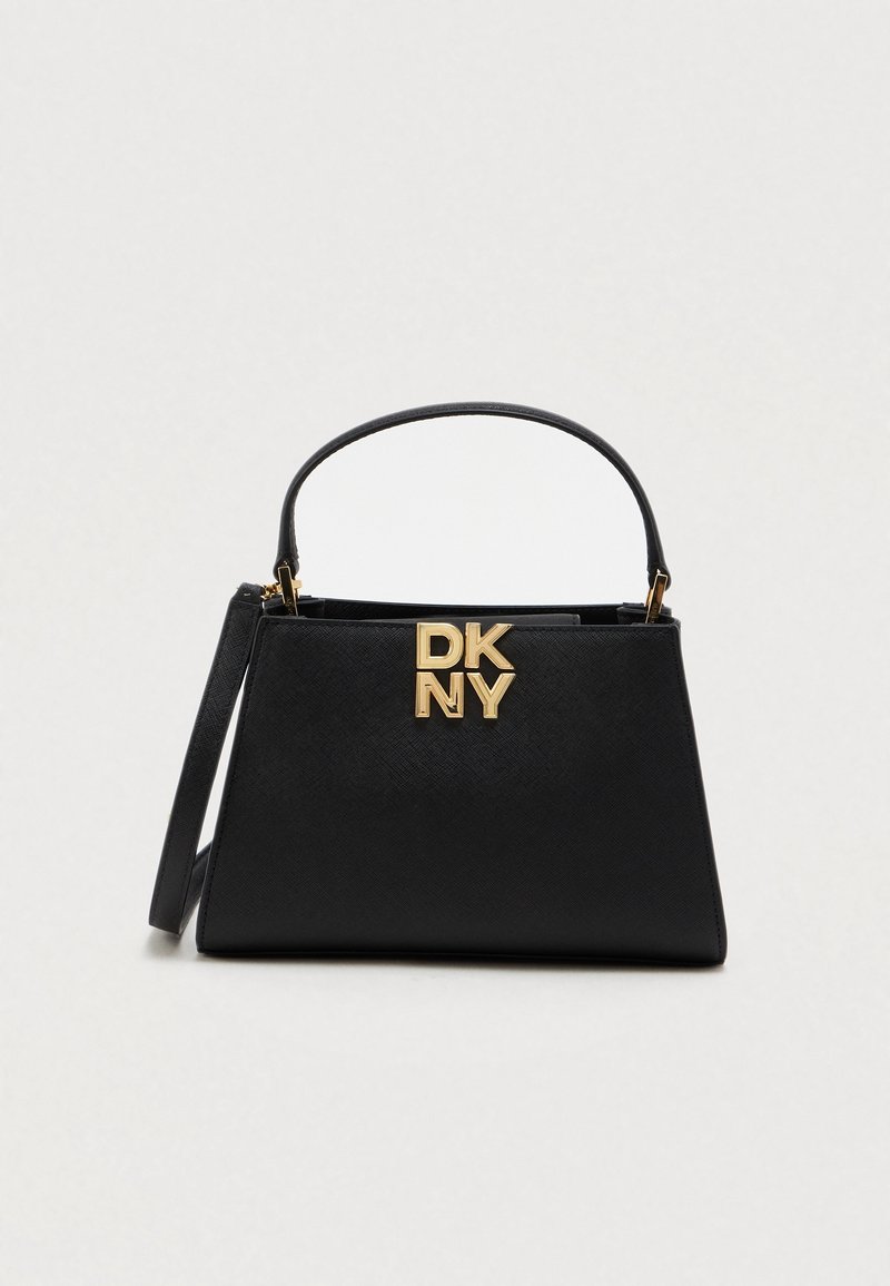 Sac à main structuré noir avec poignée supérieure, bandoulière détachable et logo DKNY doré à l'avant sur un fond clair uni.