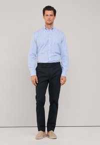 Camicia a quadri blu e bianca con bottoni abbinata a pantaloni navy; scarpe slip-on in suede marrone. Tessuto liscio e vestibilità tailored.