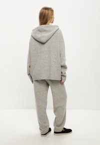 Grijze gebreide hoodie en bijpassende sweatpants, met een geribbelde zoom en manchetten, een zachte textuur en een ruime capuchon. Zwarte instappers.