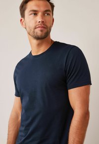 Tricou din bumbac de culoare bleumarin, cu guler rotund, mâneci scurte, formă ajustată și textură netedă, expus pe un model pe un fundal neutru.