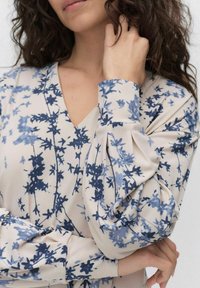 Langärmlige Bluse aus leichtem Stoff mit einem cremefarbenen Grund und blauen Blumenmuster, V-Ausschnitt und gerafften Ärmeln.