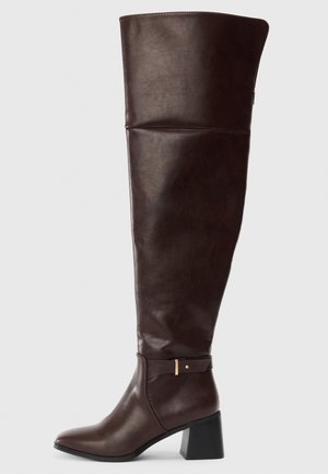 Botte haute en cuir brun foncé avec talon bloc et une petite lanière avec boucle dorée près de la cheville, vue de profil.