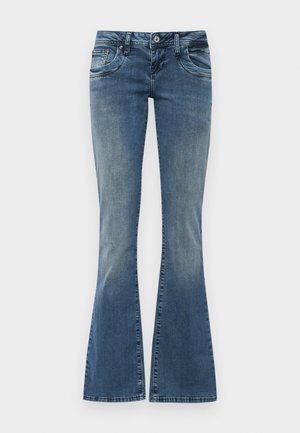 Jean évasé en denim de couleur bleue avec un effet délavé, comportant des poches avant, une fermeture à bouton et des imperfections discrètes au niveau du genou.