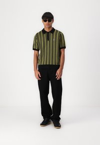 Black and yellow striped short-sleeve knit polo shirt with a collar and ribbed hem, paired with black loose-fitting pants and black sneakers.