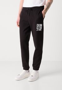 Melnas sporta bikses ar auklu jostas vietā, ar baltu "Calvin Klein Jeans" logo kreisajā augšstilbā. Mīksts audums, ar sašaurinātu kāju dizainu.