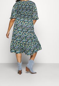 Kukallinen midi-mekko mustalla pohjalla, jossa on sinisiä ja keltaisia kukkia, puffihihoja ja kerroksellinen helma. Yhdistetty sinisiin nilkkasaappaisiin.