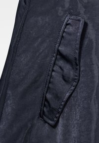 Námořnická tkanina s hladkou texturou a mírným leskem, která má postranní náprsní kapsu. Viditelné švy dodávají detail.