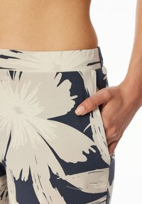 Blumenmuster-Leggings in Marineblau und Beige, aus weichem Stoff, mit dehnbarem Material und seitlichen Taschen.