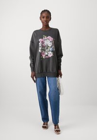 Dark gray sweatshirt with floral skull graphic, long sleeves, and ribbed hem, paired with light blue straight-leg jeans and sandals.