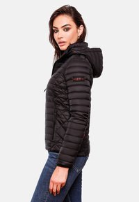 Veste de duvet noire matelassée avec capuche, poches zippées et détail de logo sur la manche, présentant un design ajusté et une texture lisse.