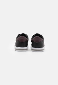 Sneaker neri in pelle sintetica con un accento bordeaux sul tallone, suola bianca e marchio "HILFIGER" sul tallone. Texture liscia, design low-profile.