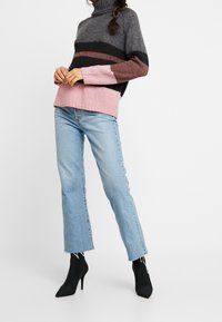 Sweter w kolorach szaro-czarnym i różowym z prążkowanym golfem. Jasnoniebieskie, postrzępione dżinsy w połączeniu z czarnymi botkami za kostkę.