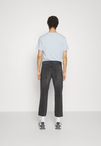Jeans de mezclilla negros con un corte relajado, costuras visibles y dos bolsillos traseros, combinados con una camiseta de manga corta de color azul claro y zapatillas.
