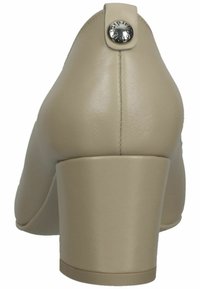 Scarpa alto in pelle beige con punta arrotondata e tacco largo. Presenta un bottone decorativo argentato sul retro. Texture liscia.