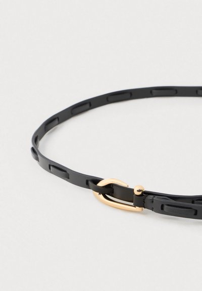 Musta nahkavyö suorakulmaisten aukkojen yksityiskohdilla ja pienellä kultaisella metallisoljella valkoista taustaa vasten.