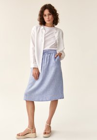 Gonna azzurro chiaro, lunga fino al ginocchio, con vita elastica e tasche. Abbinata a una camicia bianca e sandali con plateau beige. Tessuto dalla consistenza liscia.