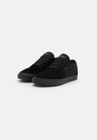 Black skate shoes made of suede and canvas. Low-top design with round toe, flat laces, and rubber outsole. Subtle brand logo on tongue.