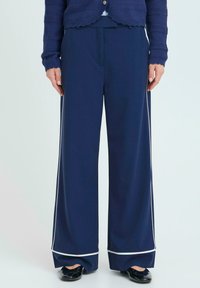 Námořnické široké kalhoty vyrobené z hladké látky, s bílým lemováním na okraji, podrobně zpracovanými předními sklady a pohodlným pasem.