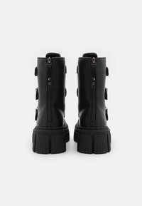 Bottes noires pour cheville à finition mate, dotées de deux fermetures éclair et cinq sangles solides. Semelle épaisse en caoutchouc texturé avec une bande de roulement prononcée.