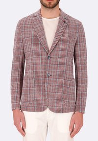 Blazer a quadri rosso e blu con rever a punta, due bottoni, tasche frontali e un tessuto texturizzato. Indossato sopra una maglietta chiara.