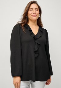 Black long-sleeve blouse with a V-neckline and textured fabric, featuring a ruffled front detail. Smooth texture and loose fit.