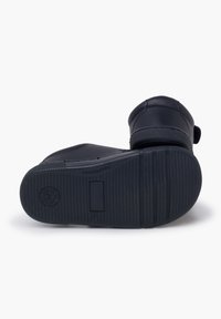 Chaussures de bébé noires avec des semelles en caoutchouc, posées vers le haut, montrant une texture antidérapante et des indications de taille sur un fond blanc.
