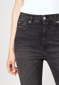 Jeans de mezclilla gris oscuro con un diseño ajustado, que cuentan con una cintura alta, cinco bolsillos y acentos de metal.