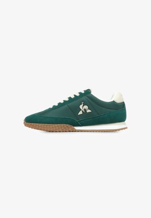 Groene sneaker met een bovenwerk van suede en glad leer, een gumrubberen outsole, witte veters en een logo met een vogelontwerp aan de zijkant.