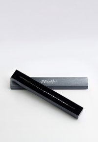 Bracciale d'argento in una scatola nera, con perle rotonde lungo una delicata catena, con una finitura lucida e il nome del marchio in rilievo sul coperchio.